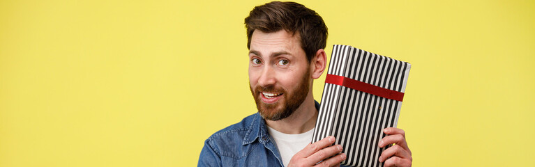 Handsome smiling man shaking gift box and looking at camera. Great present