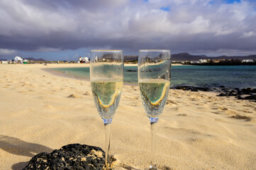 Two glasses of white champagne or cava sparkling wine served on white sandy tropical beach and blue ocean, romantic vacation, winter sun on Fuerteventura, Canary, Spain