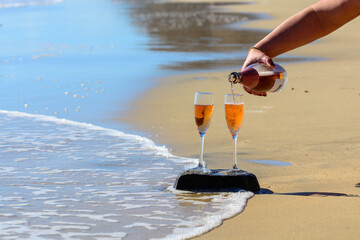 Two glasses of rose champagne or cava sparkling wine served on white sandy tropical beach and blue...