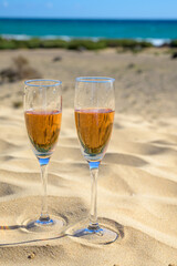 Two glasses of rose champagne or cava sparkling wine served on white sandy tropical beach with dunes and blue ocean, romantic vacation, winter sun on Fuerteventura, Canary, Spain