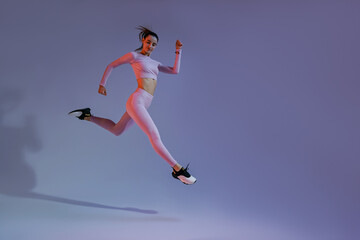 Fototapeta na wymiar Athletic active woman jumping on studio background. Dynamic movement