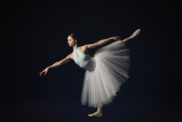 Young ballerina practicing dance moves on black background