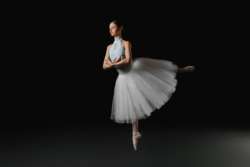 Fototapeta premium Young ballerina practicing dance moves on black background