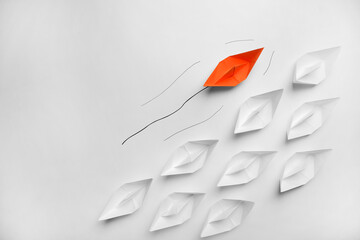 Orange paper boat floating past others on white background, flat lay with space for text. Uniqueness concept