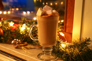 Glass of delicious hot cocoa with marshmallows and Christmas decoration on windowsill