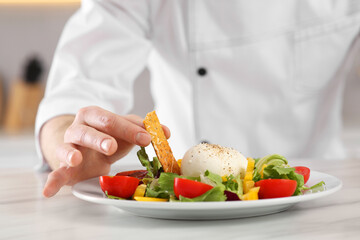 Professional chef decorating delicious salad with crispy bread at marble table, closeup