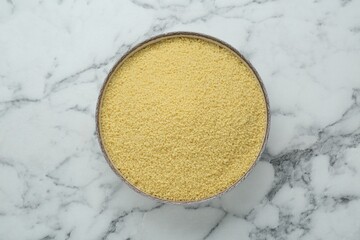Bowl of raw couscous on white marble table, top view