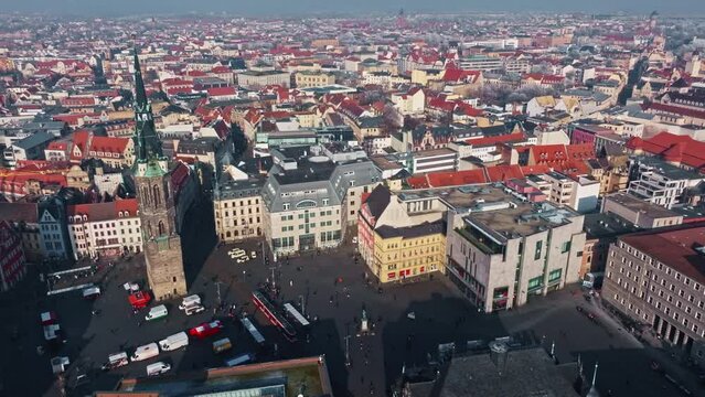 Drone shot revealing Red Tower (Roter Turm) in Market Square Halle (Marktplatz ) . Central town plaza featuring a clock tower, historic buildings, shops, cafes, Tramway & a stage for events.