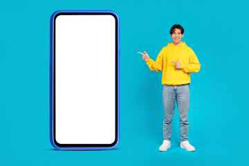 Asian Teen Boy Pointing At Big Phone On Blue Background