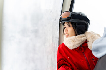 Young Asian woman rises to snowy mountain peak on cableway ski lift for practicing snowboarding at...
