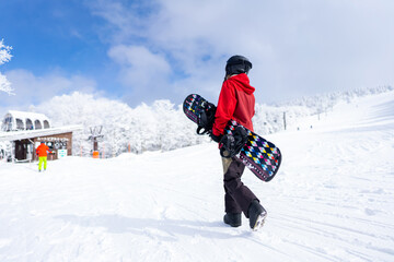 Fototapeta na wymiar Young Asian woman holding snowboard walking on snowy mountain at in ski resort. Attractive girl enjoy outdoor active lifestyle extreme sport training freeride snowboarding on winter holiday vacation.