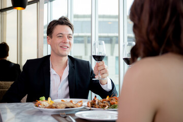 Happy young couple holding with glass of wine together in anniversary at restaurant for celebration, man and woman dinning while date with romance and relationship, valentine and holiday concept.
