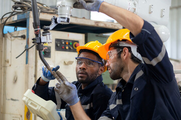Two engineer man working with machine robot automatic together at factory, technician maintenance and improvement while examining ai of robot and control with remote, industry and innovation concept.