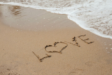 Love lettering on the sandy beach and sea water