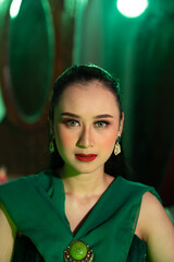 close up photo of an Asian woman with a full face of makeup and wearing green clothes and jewelry...