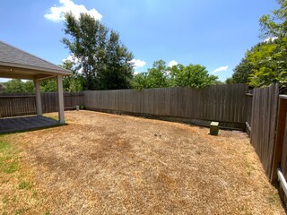 American home backyard with a wood fence around and some dead grass.