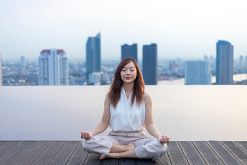 Woman relaxingly practicing meditation at the swimming pool rooftop with the view of urban skyline building to attain happiness from inner peace wisdom concept