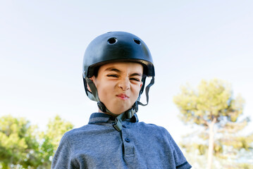 Little boy looking at camera while wearing protective helmet outdoors in a park.