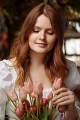 A young female florist in white clothes works in an authentic flower shop, making bouquets in a flower shop. Workplace of a flower shop employee.