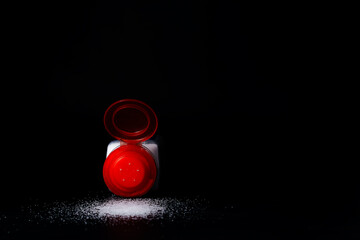 red salt shaker with salt spilled on black table