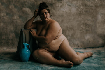 portrait of a nude plus size woman sitting on the ground leaning on a box beside a blue vase - Powered by Adobe