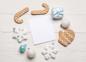 Paper sheet, gift, cookies and Christmas decor on white wooden background