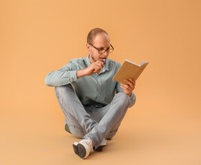 Young man in eyeglasses with disposable electronic cigarette reading book on beige background