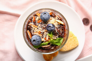 Glass of delicious chocolate pudding with blueberry, almond and cookie on pink napkin