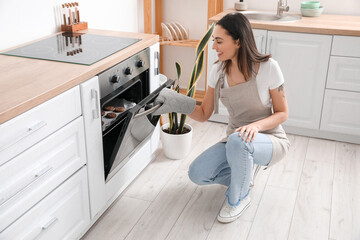 Young woman opening electric oven in kitchen