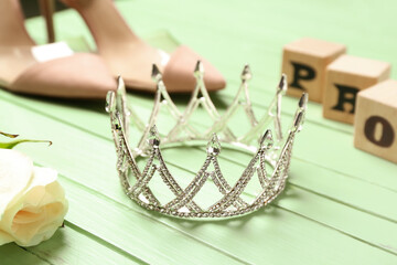 Beautiful tiara and rose on green wooden table, closeup. Prom concept