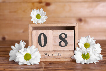 Cube calendar with date MARCH 8 and beautiful chamomile flowers on wooden table. Women's Day celebration