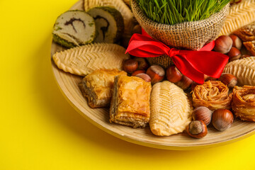 Plate with treats and grass on yellow background, closeup. Novruz Bayram celebration