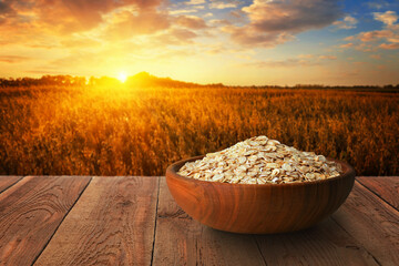oat flakes in bowl on table with ripe cereal field on sunset as background