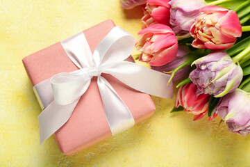 Gift box and beautiful tulip flowers on yellow background. Hello spring