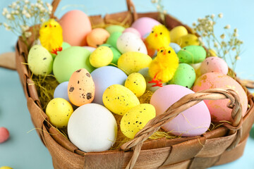 Basket with different Easter eggs, toy chicks and gypsophila flowers on color background, closeup