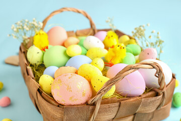 Basket with different Easter eggs, toy chicks and gypsophila flowers on color background, closeup