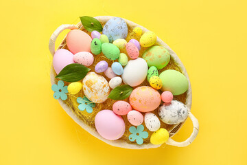 Fototapeta na wymiar Basket with beautiful Easter eggs and plant leaves on yellow background