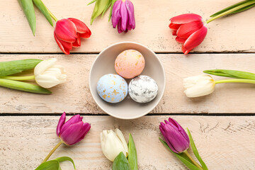 Composition with bowl of painted Easter eggs and beautiful tulip flowers on light wooden background