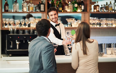 Bar, barman and serve a couple alcohol drinks on a date with hospitality, happy and smile at a hotel. Waiter, bartender and server help customers or people with good service for a celebration - obrazy, fototapety, plakaty