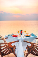 Seascape view under sunset light with dining table with infinity pool around. Romantic tranquil getaway for two, couple concept. Chairs, food and romance. Luxury destination dining, honeymoon template