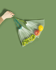 Hand holding reusable grocery bags from net, reusable packaging with fruits, grape, lemon, apple,...