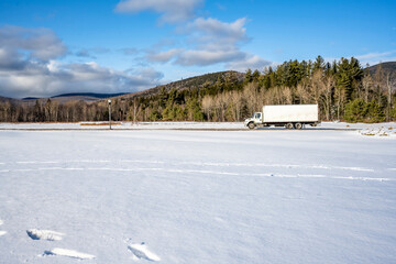 Winter view with covered by snow field and day cab semi truck with box trailer driving on the local road making cargo delivery