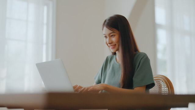 Smiling asian young woman working on laptop at home office. Young asian student using computer remote studying, virtual training, e-learning, watching online education webinar at house