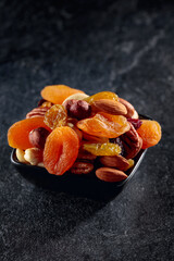 Dried fruits and nuts on a black stone table.