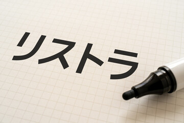 リストラと書かれたノートとマーカー