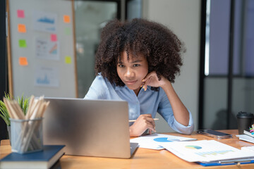 Smiling African American businesswoman working on a laptop sitting at her desk in a modern office.