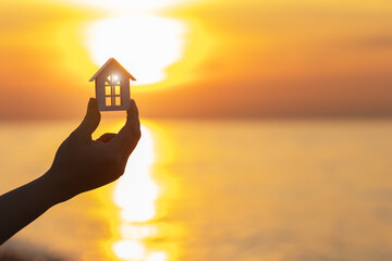renting an apartment by the sea, hand holding a house against the background of a sea sunset