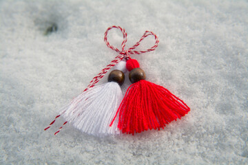 Closeup of a red and white martenitsa (martisol) with wooden beads sitting on the snow. Martenitsa...