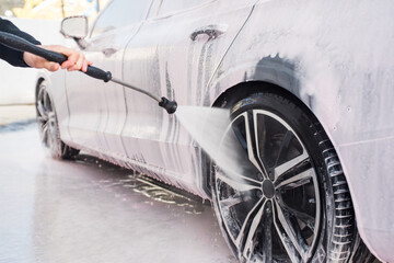 Side view of worker cleaning the tire and the rim of the car with sprayer water pressure. Close up concept of washing car.