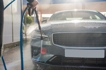 Detail of a person cleaning a car at a service station. Front view of a worker cleaning the vehicle.